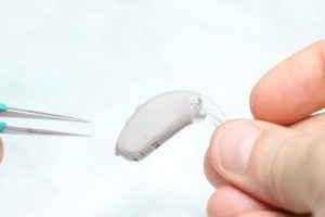 Hand holding a hearing aid with tweezers in the other hand