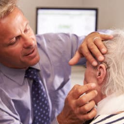 Audiologist fitting a senior female patient with a hearing aid