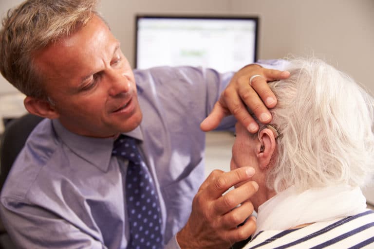 Audiologist fitting a senior female patient with a hearing aid