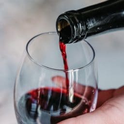 A bottle of red wine being poured into a glass.